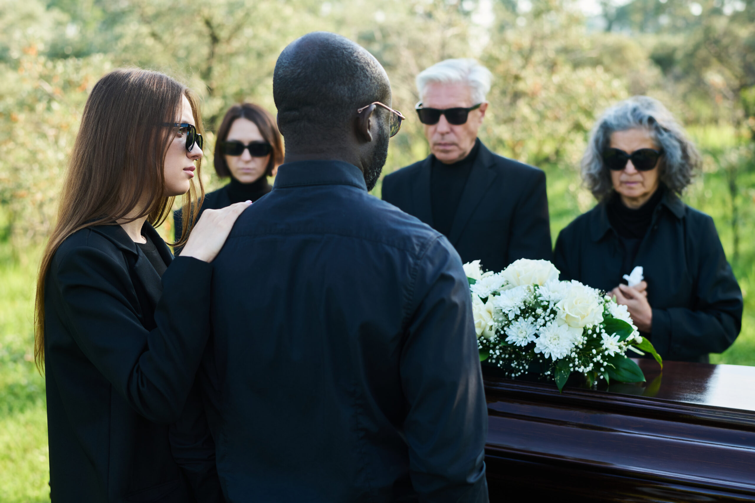 Back view of young woman in mourning attire supporting her husband at funeral